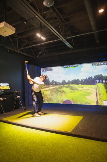 A player mid-swing in the private Full Swing simulator bay